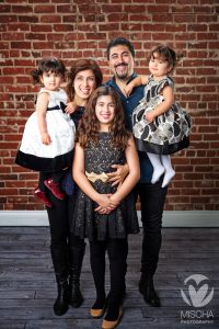 Family portrait of two adults holding toddlers and an older girl standing in front, all dressed formally.
