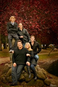 Five people posing on rocks in a park with red autumn leaves by a water edge.