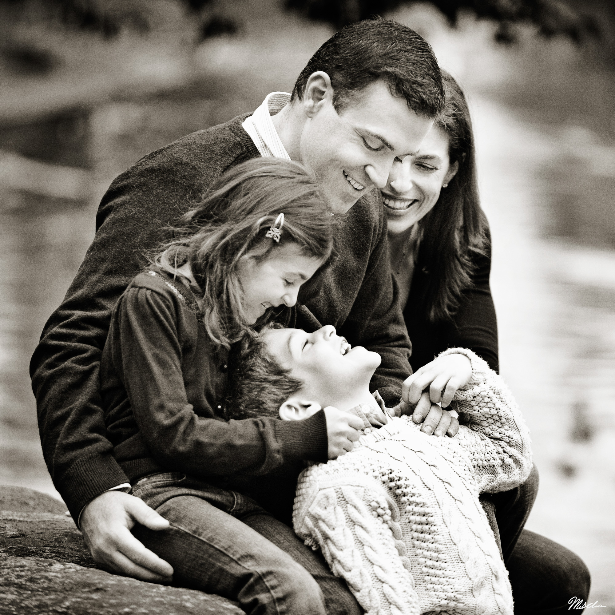 Black and white photo of a family of four laughing and embracing outdoors.