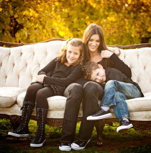 Woman with two children sitting on a cream sofa outdoors with autumn leaves in the background.