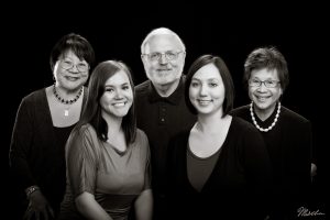 Black and white portrait of five smiling adults against a plain dark background.