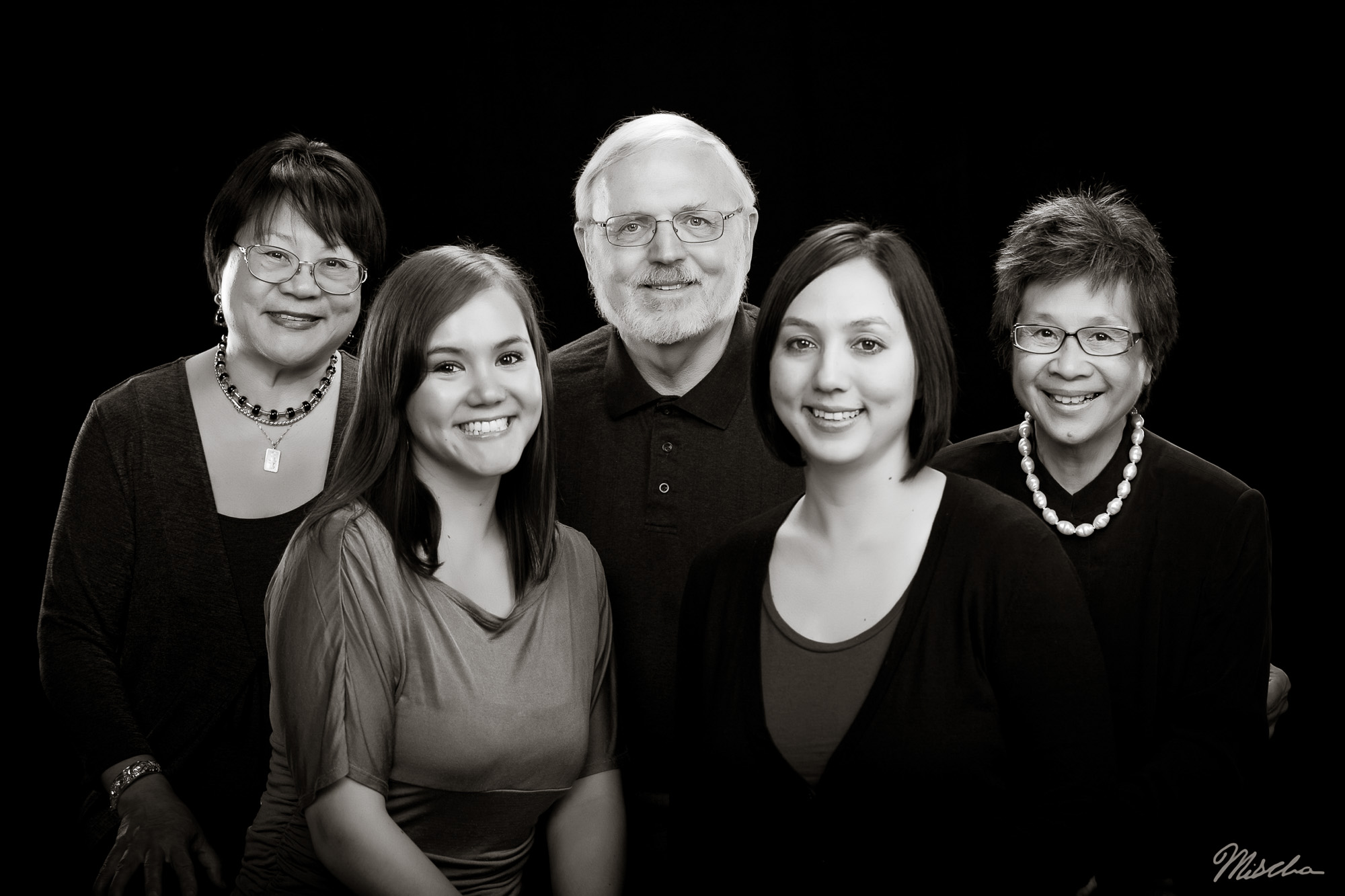 Black and white portrait of five smiling adults against a plain dark background.