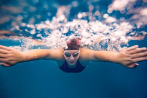 Underwater view of a swimmer in a cap and goggles extending arms forward with bubbles around.