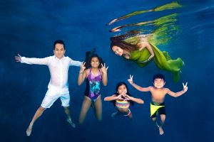 Underwater photo of a man in white, a woman in green dress, and three children in swimsuits posing.