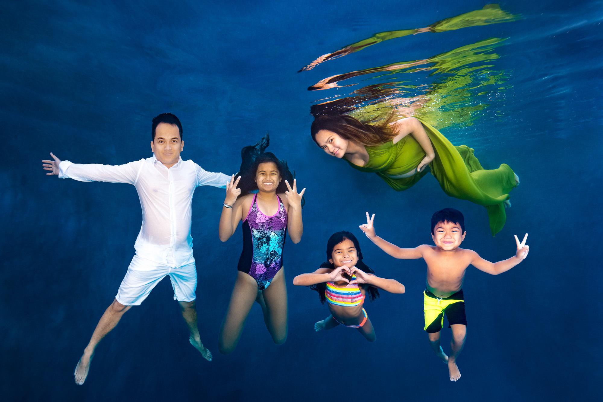 Underwater photo of a man in white, a woman in green dress, and three children in swimsuits posing.