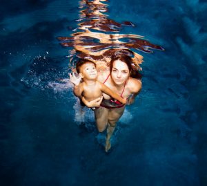 Underwater view of a woman in a red bikini holding a young child in clear blue water.
